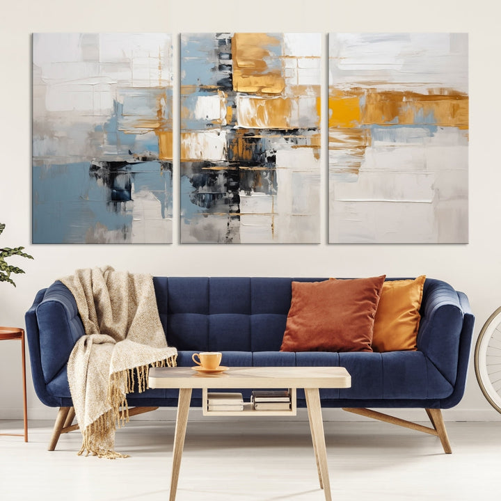 A stunning triptych of the Blue Orange Abstract Wall Art Canvas Print adorns the wall. These gallery-wrapped abstract pieces, showcasing blue, yellow, and white tones, feature a UV-protective coating to maintain their vivid colors.