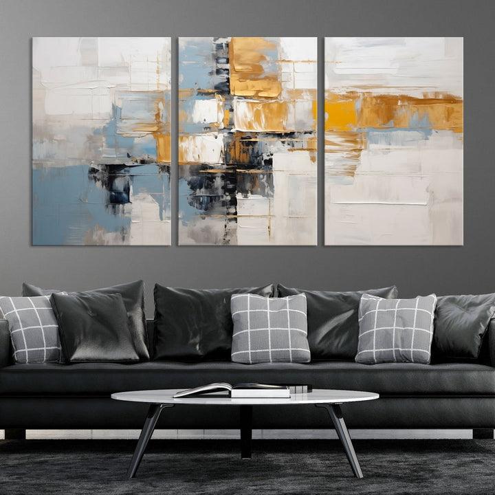 A stunning triptych of the Blue Orange Abstract Wall Art Canvas Print adorns the wall. These gallery-wrapped abstract pieces, showcasing blue, yellow, and white tones, feature a UV-protective coating to maintain their vivid colors.