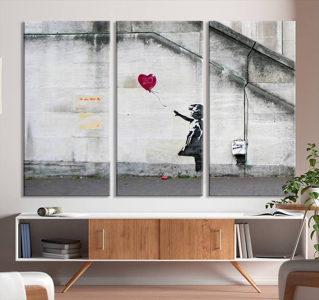 The "Girl with a Balloon Banksy Street Graffiti Art Canvas Print" is a gallery-quality wall art piece that features an image of a girl releasing a heart-shaped balloon. Handmade in the USA, this canvas artwork brings charm and emotion to any room.