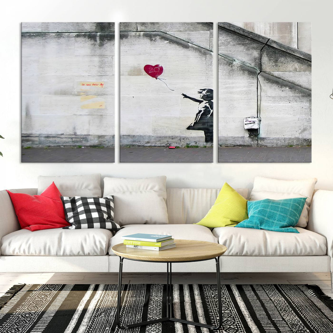 The "Girl with a Balloon Banksy Street Graffiti Art Canvas Print" is a gallery-quality wall art piece that features an image of a girl releasing a heart-shaped balloon. Handmade in the USA, this canvas artwork brings charm and emotion to any room.