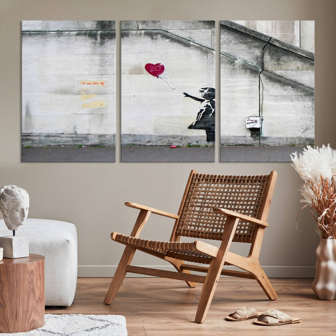 The "Girl with a Balloon Banksy Street Graffiti Art Canvas Print" is a gallery-quality wall art piece that features an image of a girl releasing a heart-shaped balloon. Handmade in the USA, this canvas artwork brings charm and emotion to any room.