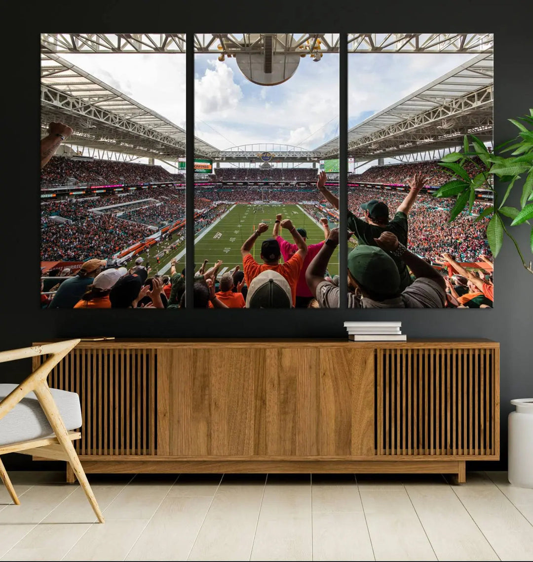 The living room features handmade triptych wall art crafted in the USA, depicting a cheering crowd at a Miami Hurricanes football game. The artwork showcases the Miami Hard Rock Stadium on premium canvas.