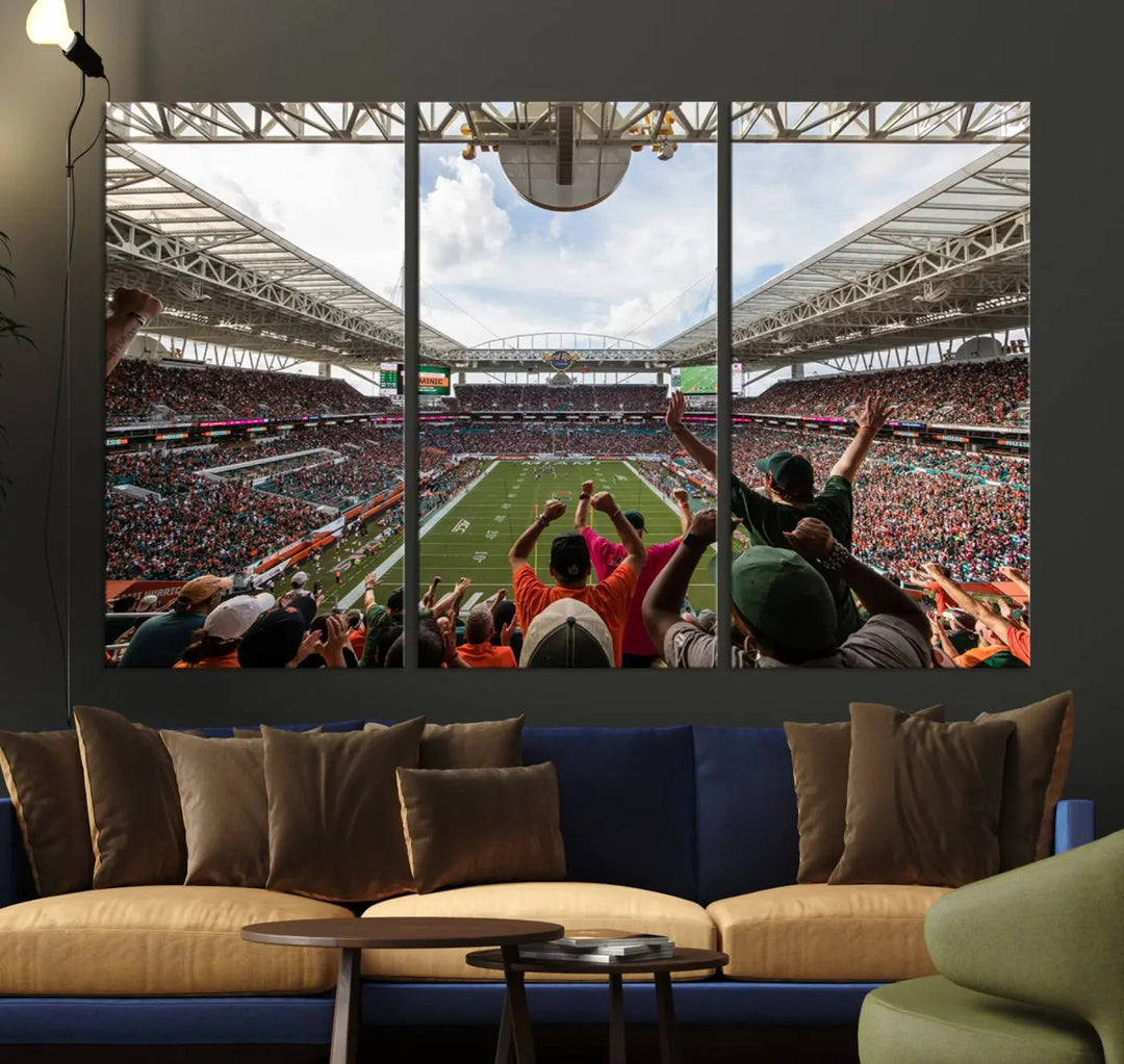 The living room features handmade triptych wall art crafted in the USA, depicting a cheering crowd at a Miami Hurricanes football game. The artwork showcases the Miami Hard Rock Stadium on premium canvas.