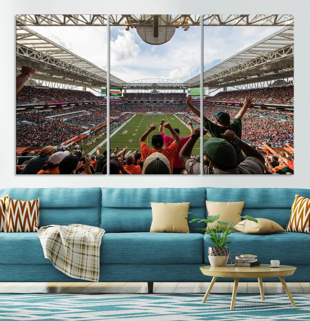 The living room features handmade triptych wall art crafted in the USA, depicting a cheering crowd at a Miami Hurricanes football game. The artwork showcases the Miami Hard Rock Stadium on premium canvas.