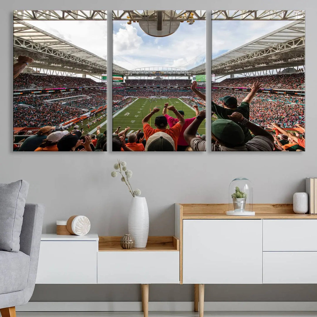 The living room features handmade triptych wall art crafted in the USA, depicting a cheering crowd at a Miami Hurricanes football game. The artwork showcases the Miami Hard Rock Stadium on premium canvas.