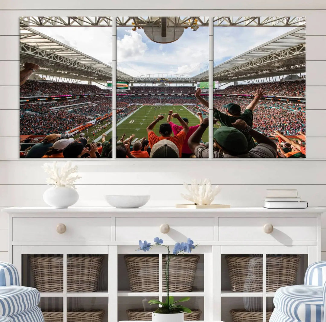 The living room features handmade triptych wall art crafted in the USA, depicting a cheering crowd at a Miami Hurricanes football game. The artwork showcases the Miami Hard Rock Stadium on premium canvas.