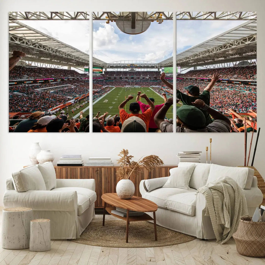 The living room features handmade triptych wall art crafted in the USA, depicting a cheering crowd at a Miami Hurricanes football game. The artwork showcases the Miami Hard Rock Stadium on premium canvas.