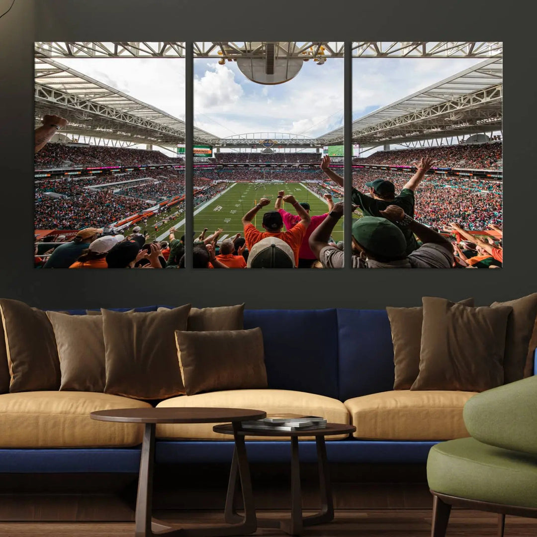 The living room features handmade triptych wall art crafted in the USA, depicting a cheering crowd at a Miami Hurricanes football game. The artwork showcases the Miami Hard Rock Stadium on premium canvas.