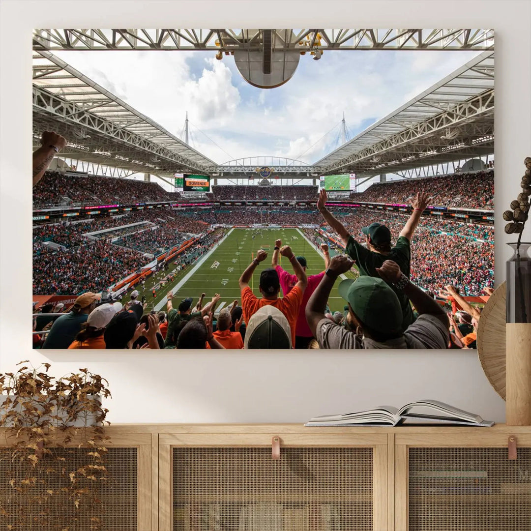 The living room features handmade triptych wall art crafted in the USA, depicting a cheering crowd at a Miami Hurricanes football game. The artwork showcases the Miami Hard Rock Stadium on premium canvas.