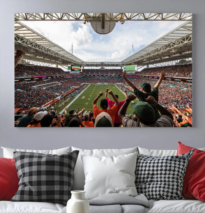 The living room features handmade triptych wall art crafted in the USA, depicting a cheering crowd at a Miami Hurricanes football game. The artwork showcases the Miami Hard Rock Stadium on premium canvas.