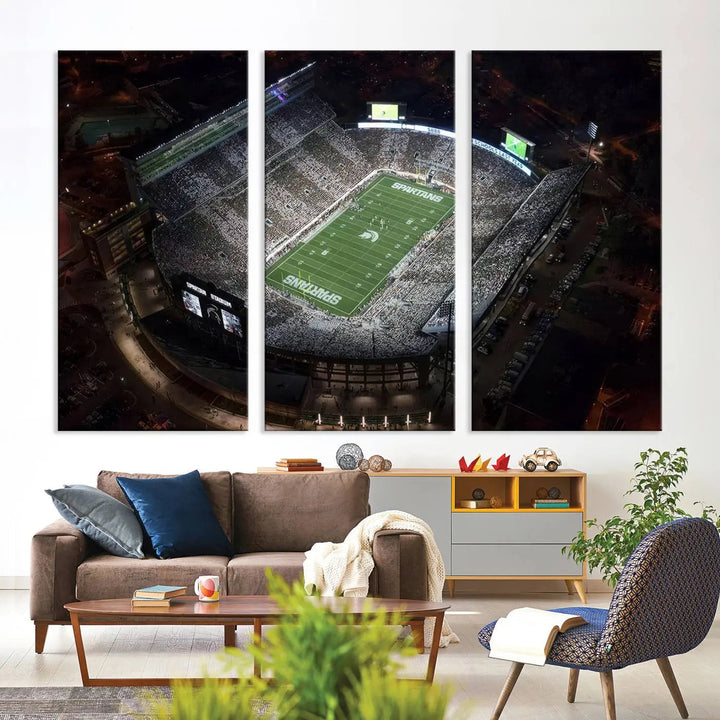 The "Michigan State Spartans Football Team Print - East Lansing Spartan Stadium Wall Art Canvas Print" is elegantly displayed on a wall, showcasing a brightly lit football stadium at night with a gallery-quality finish.