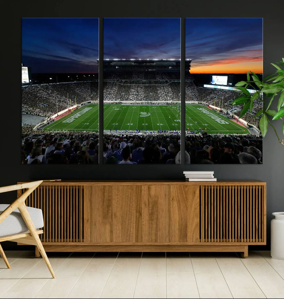 The room showcases a triptych wall art featuring the Michigan State Spartans football team at East Lansing Spartan Stadium at dusk, elegantly printed on premium canvas for a gallery-quality finish.