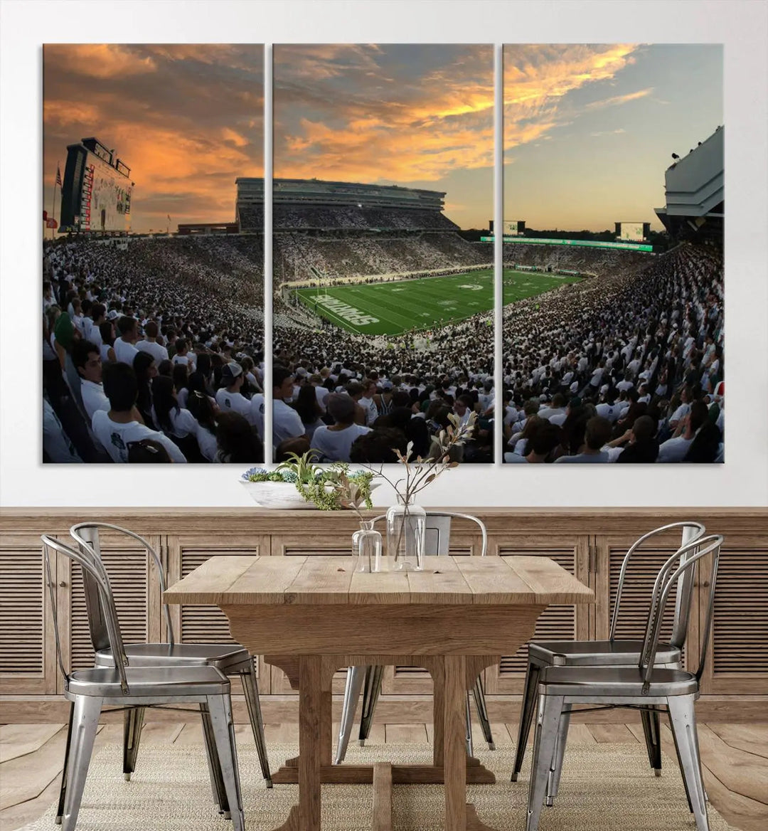 A living room showcasing a stunning Michigan State Spartans Football Team Print on a three-panel canvas, depicting the bustling Spartan Stadium in East Lansing at sunset, all handmade in the USA.