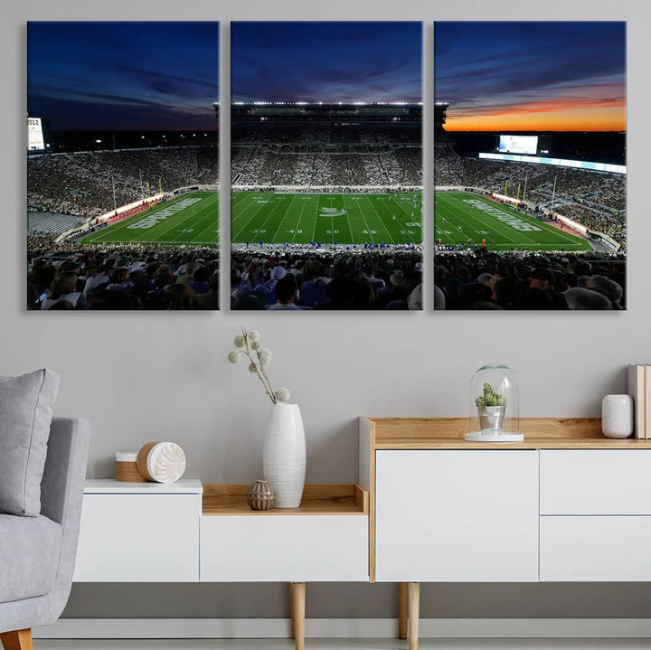 The room showcases a triptych wall art featuring the Michigan State Spartans football team at East Lansing Spartan Stadium at dusk, elegantly printed on premium canvas for a gallery-quality finish.