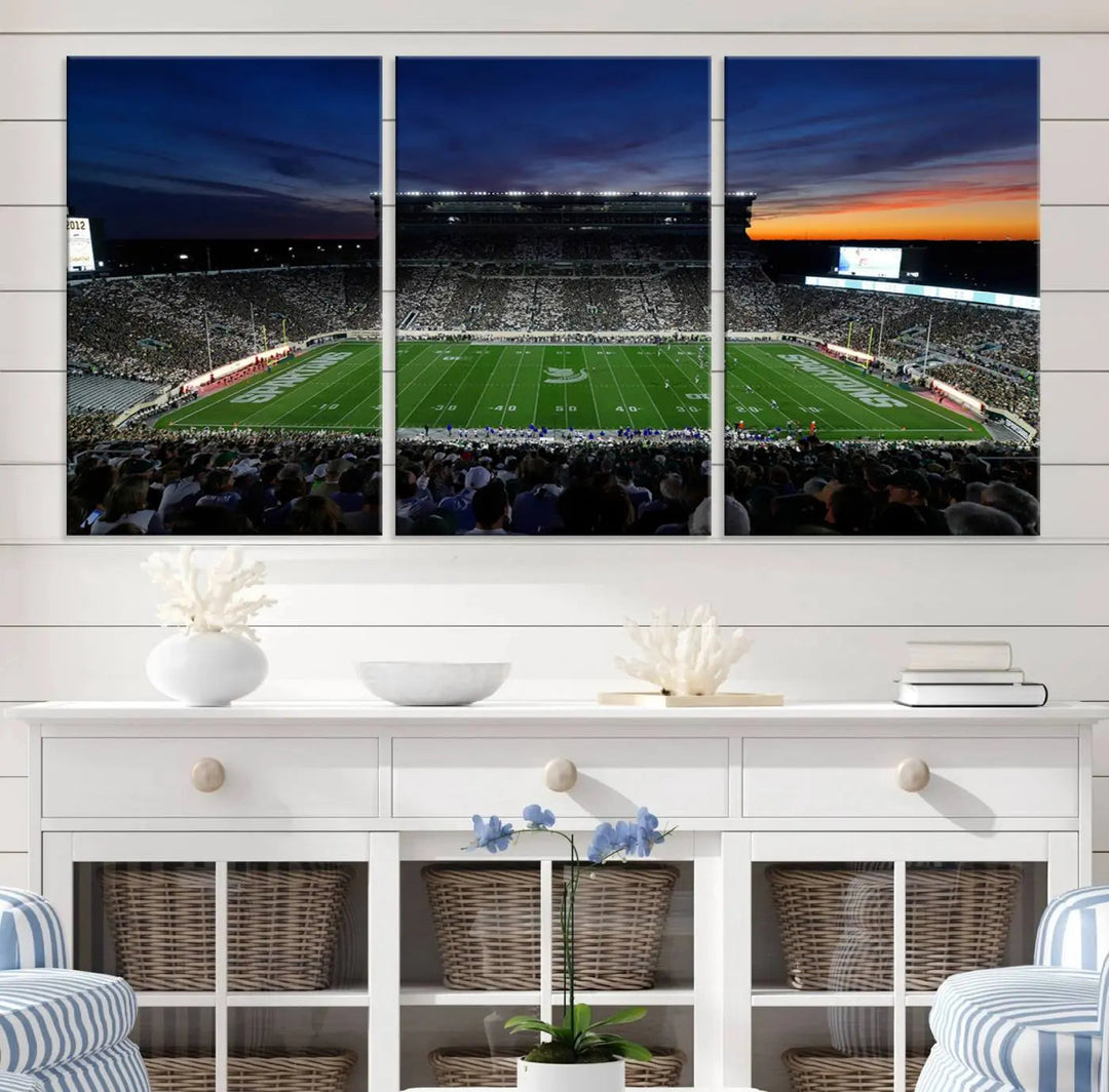 The room showcases a triptych wall art featuring the Michigan State Spartans football team at East Lansing Spartan Stadium at dusk, elegantly printed on premium canvas for a gallery-quality finish.