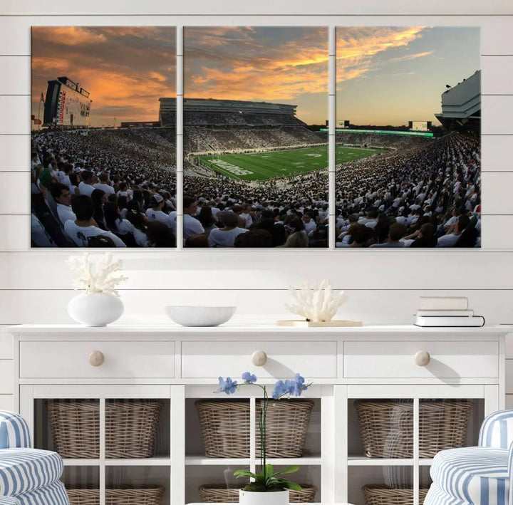 A living room showcasing a stunning Michigan State Spartans Football Team Print on a three-panel canvas, depicting the bustling Spartan Stadium in East Lansing at sunset, all handmade in the USA.