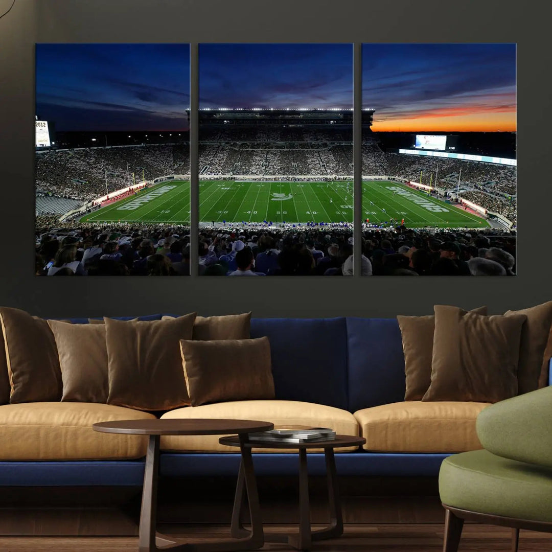 The room showcases a triptych wall art featuring the Michigan State Spartans football team at East Lansing Spartan Stadium at dusk, elegantly printed on premium canvas for a gallery-quality finish.