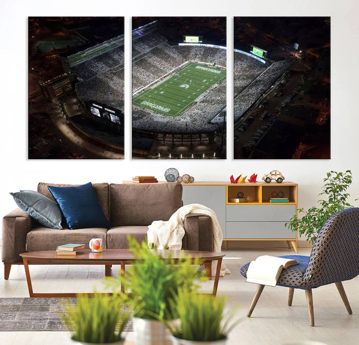 The "Michigan State Spartans Football Team Print - East Lansing Spartan Stadium Wall Art Canvas Print" is elegantly displayed on a wall, showcasing a brightly lit football stadium at night with a gallery-quality finish.