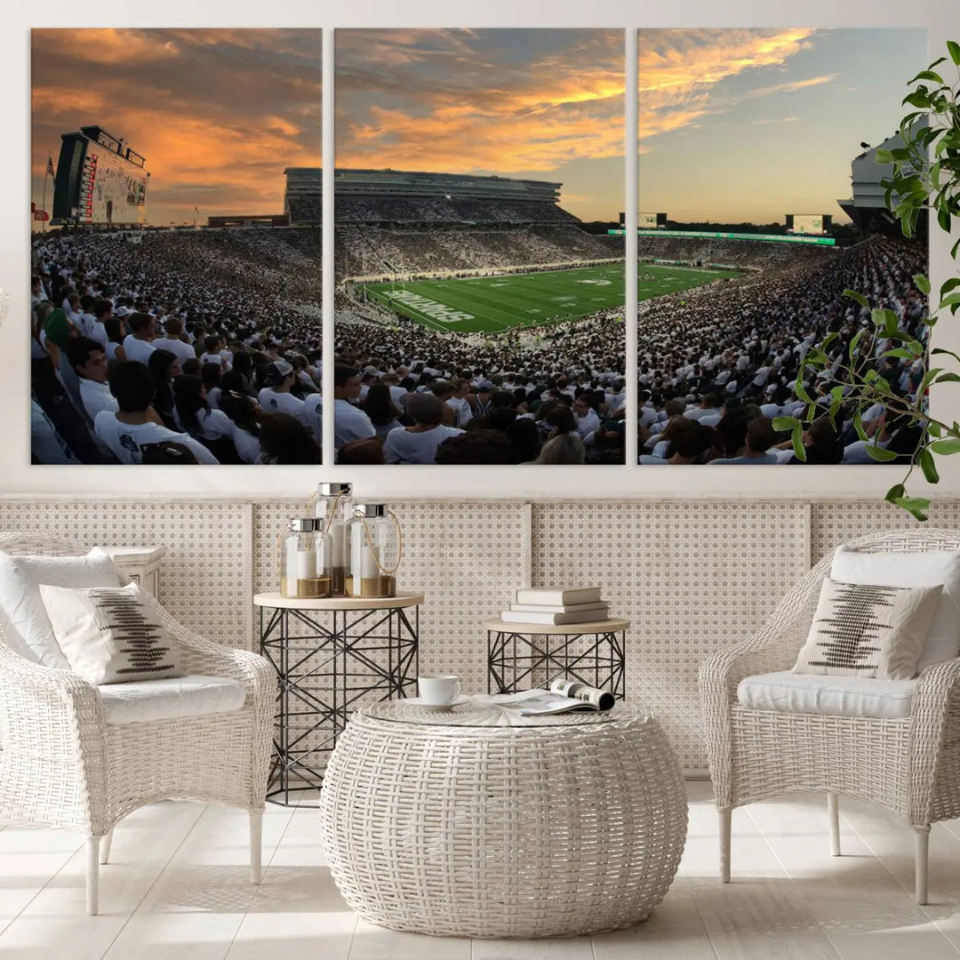 A living room showcasing a stunning Michigan State Spartans Football Team Print on a three-panel canvas, depicting the bustling Spartan Stadium in East Lansing at sunset, all handmade in the USA.