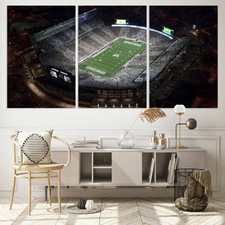 The "Michigan State Spartans Football Team Print - East Lansing Spartan Stadium Wall Art Canvas Print" is elegantly displayed on a wall, showcasing a brightly lit football stadium at night with a gallery-quality finish.