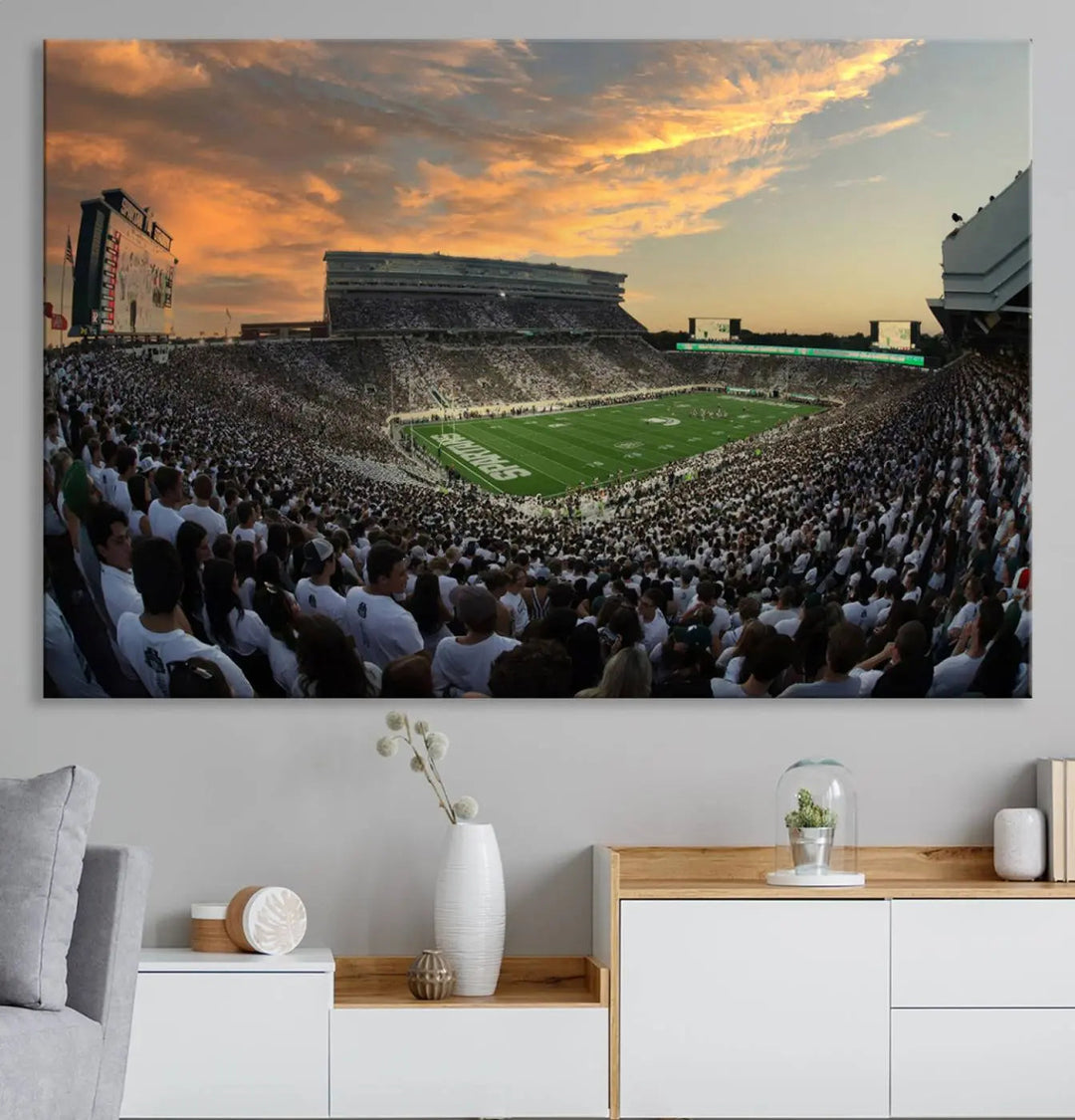 A living room showcasing a stunning Michigan State Spartans Football Team Print on a three-panel canvas, depicting the bustling Spartan Stadium in East Lansing at sunset, all handmade in the USA.