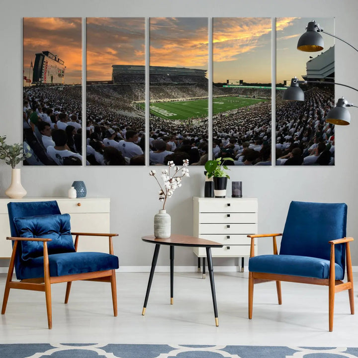 A living room showcasing a stunning Michigan State Spartans Football Team Print on a three-panel canvas, depicting the bustling Spartan Stadium in East Lansing at sunset, all handmade in the USA.