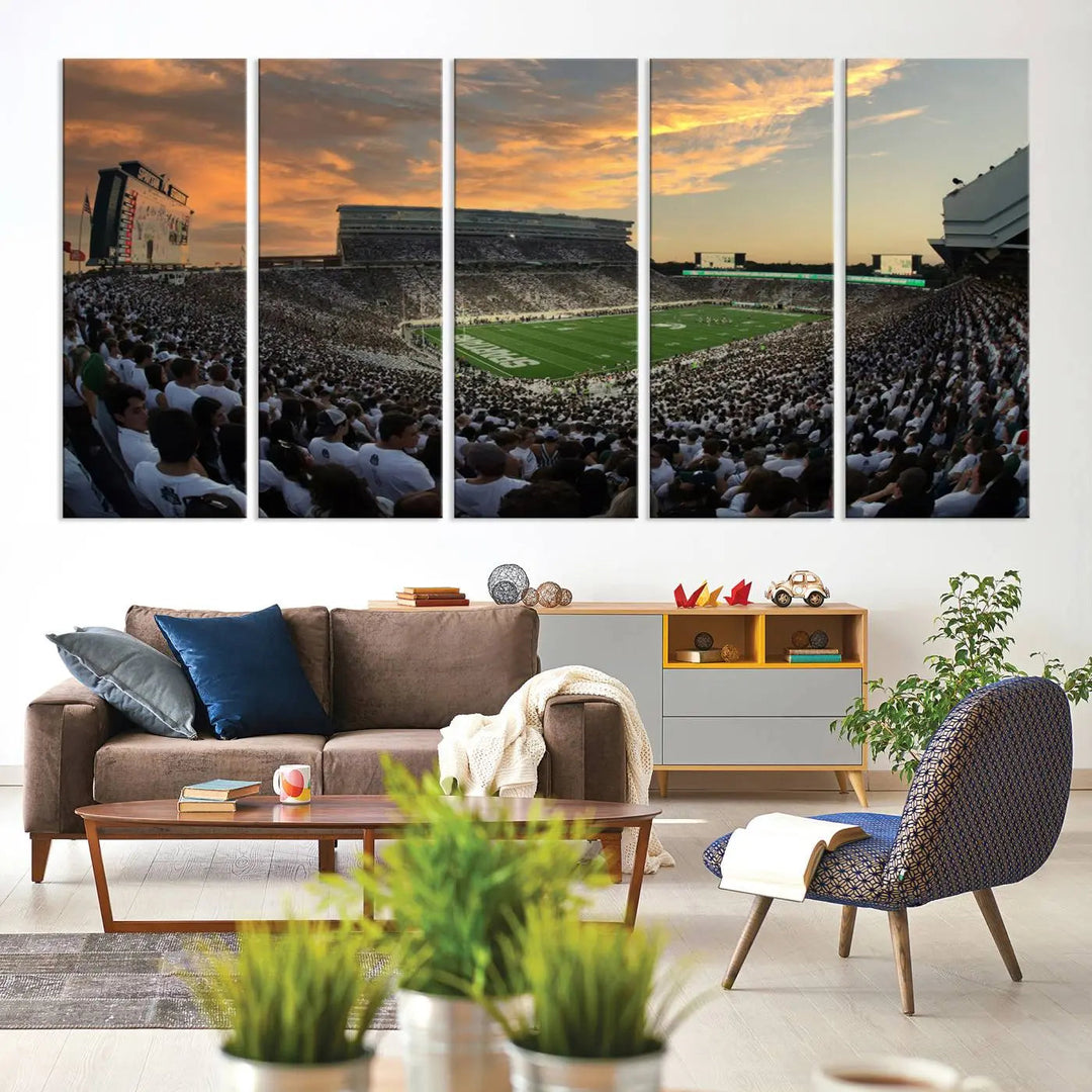 A living room showcasing a stunning Michigan State Spartans Football Team Print on a three-panel canvas, depicting the bustling Spartan Stadium in East Lansing at sunset, all handmade in the USA.