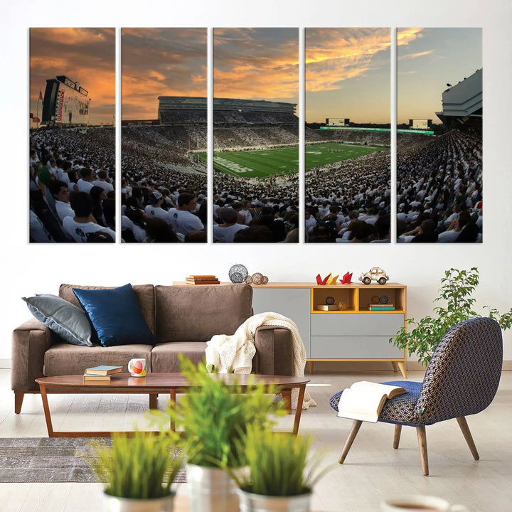 A living room showcasing a stunning Michigan State Spartans Football Team Print on a three-panel canvas, depicting the bustling Spartan Stadium in East Lansing at sunset, all handmade in the USA.