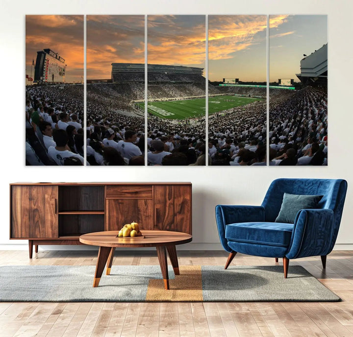 A living room showcasing a stunning Michigan State Spartans Football Team Print on a three-panel canvas, depicting the bustling Spartan Stadium in East Lansing at sunset, all handmade in the USA.