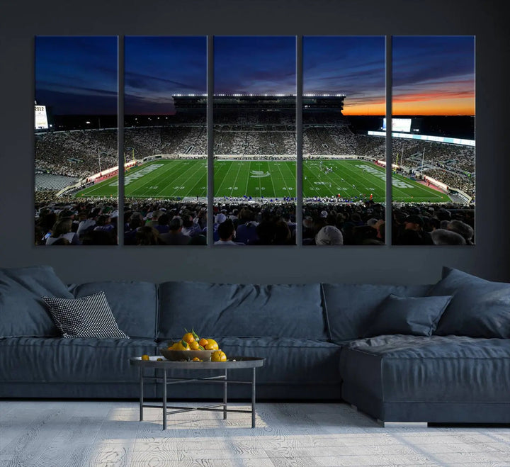 The room showcases a triptych wall art featuring the Michigan State Spartans football team at East Lansing Spartan Stadium at dusk, elegantly printed on premium canvas for a gallery-quality finish.