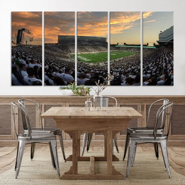 A living room showcasing a stunning Michigan State Spartans Football Team Print on a three-panel canvas, depicting the bustling Spartan Stadium in East Lansing at sunset, all handmade in the USA.