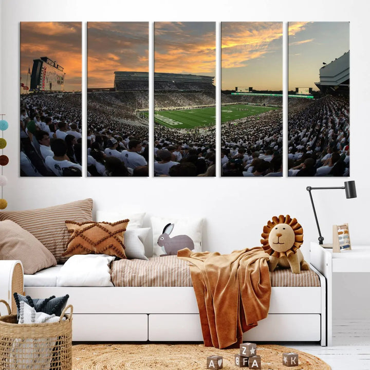 A living room showcasing a stunning Michigan State Spartans Football Team Print on a three-panel canvas, depicting the bustling Spartan Stadium in East Lansing at sunset, all handmade in the USA.