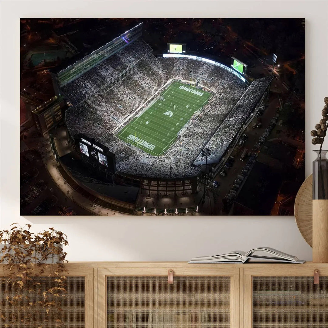 The "Michigan State Spartans Football Team Print - East Lansing Spartan Stadium Wall Art Canvas Print" is elegantly displayed on a wall, showcasing a brightly lit football stadium at night with a gallery-quality finish.