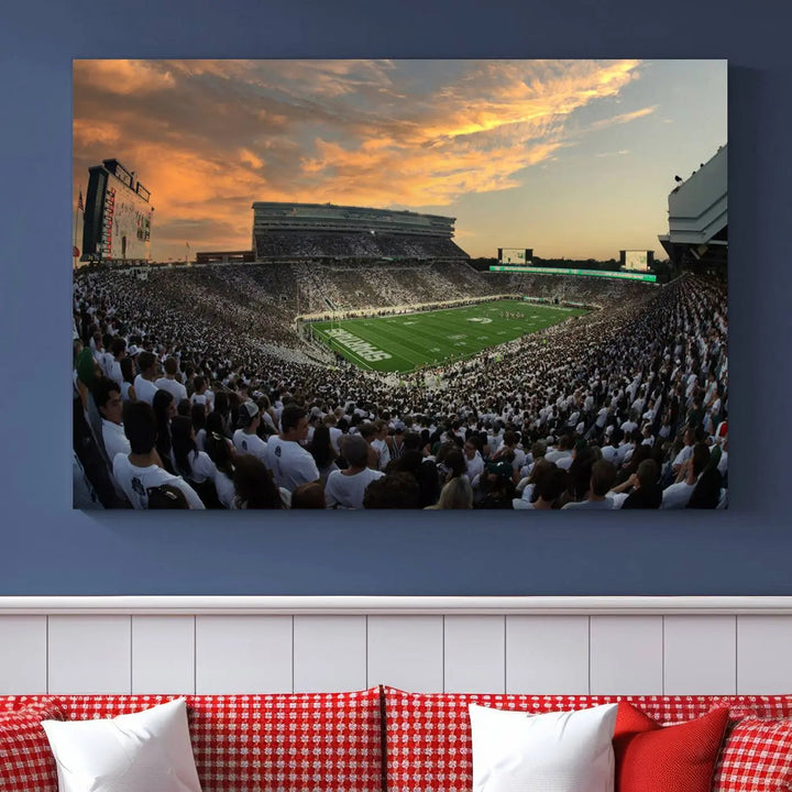 A living room showcasing a stunning Michigan State Spartans Football Team Print on a three-panel canvas, depicting the bustling Spartan Stadium in East Lansing at sunset, all handmade in the USA.