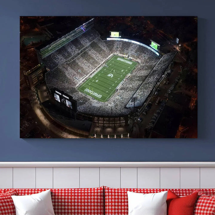 The "Michigan State Spartans Football Team Print - East Lansing Spartan Stadium Wall Art Canvas Print" is elegantly displayed on a wall, showcasing a brightly lit football stadium at night with a gallery-quality finish.