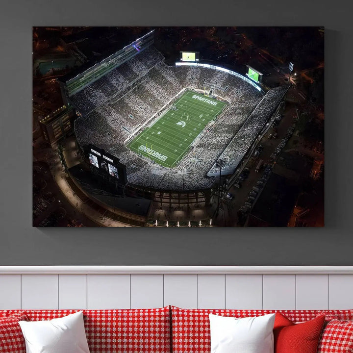 The "Michigan State Spartans Football Team Print - East Lansing Spartan Stadium Wall Art Canvas Print" is elegantly displayed on a wall, showcasing a brightly lit football stadium at night with a gallery-quality finish.