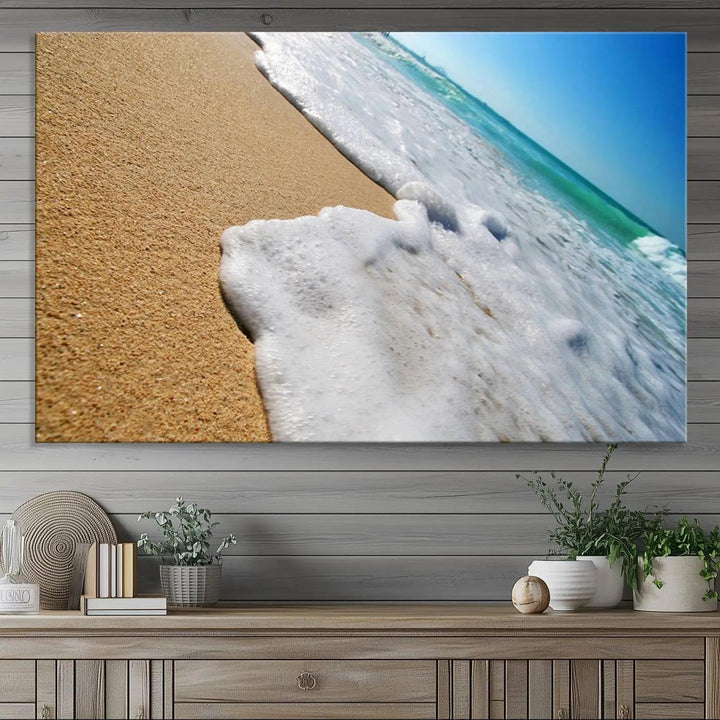 The Sandy Shoreline Close-Up Ocean Wave Canvas Print, depicting waves washing onto the sand, adorns the wall.