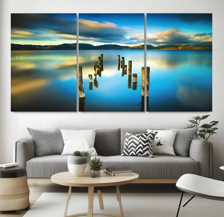 A triptych of a serene lake scene with old wooden pillars, blue sky, and clouds casts a coastal ambiance. The Sea Ocean Sunset Beach Wall Art Canvas Print reflects the soothing nature of the ocean.