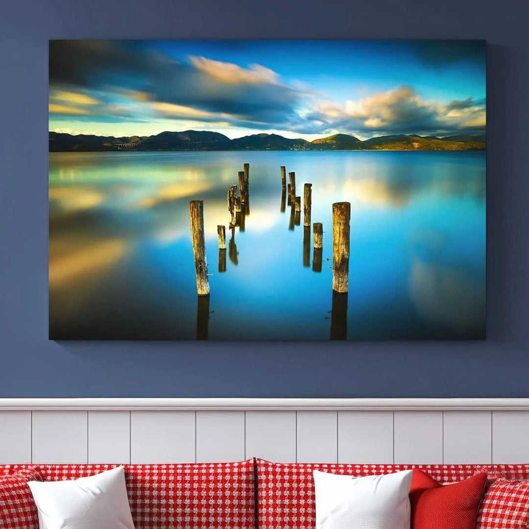 A triptych of a serene lake scene with old wooden pillars, blue sky, and clouds casts a coastal ambiance. The Sea Ocean Sunset Beach Wall Art Canvas Print reflects the soothing nature of the ocean.