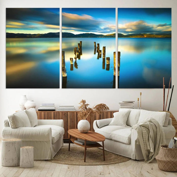 A triptych of a serene lake scene with old wooden pillars, blue sky, and clouds casts a coastal ambiance. The Sea Ocean Sunset Beach Wall Art Canvas Print reflects the soothing nature of the ocean.