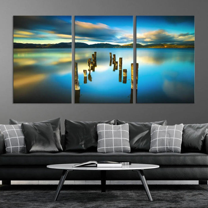 A triptych of a serene lake scene with old wooden pillars, blue sky, and clouds casts a coastal ambiance. The Sea Ocean Sunset Beach Wall Art Canvas Print reflects the soothing nature of the ocean.