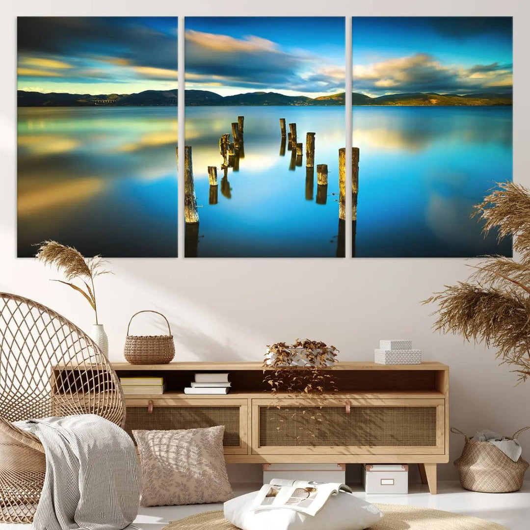 A triptych of a serene lake scene with old wooden pillars, blue sky, and clouds casts a coastal ambiance. The Sea Ocean Sunset Beach Wall Art Canvas Print reflects the soothing nature of the ocean.