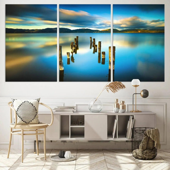 A triptych of a serene lake scene with old wooden pillars, blue sky, and clouds casts a coastal ambiance. The Sea Ocean Sunset Beach Wall Art Canvas Print reflects the soothing nature of the ocean.