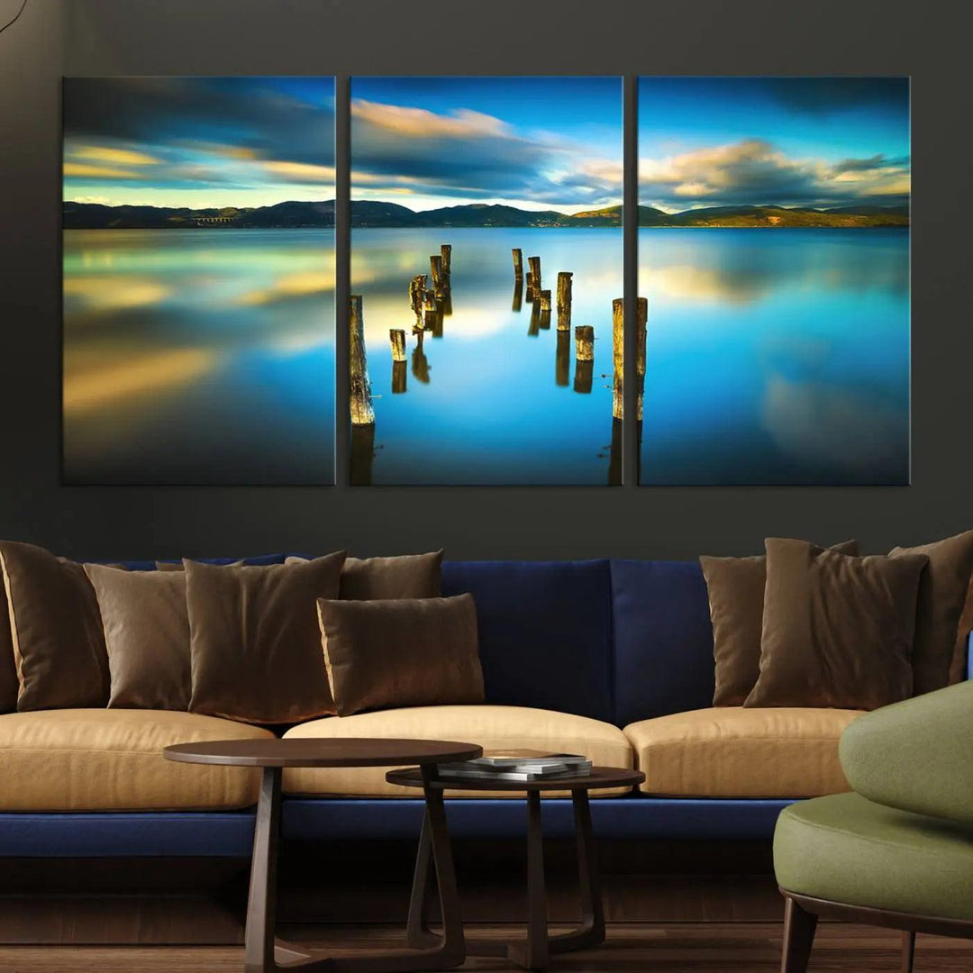 A triptych of a serene lake scene with old wooden pillars, blue sky, and clouds casts a coastal ambiance. The Sea Ocean Sunset Beach Wall Art Canvas Print reflects the soothing nature of the ocean.