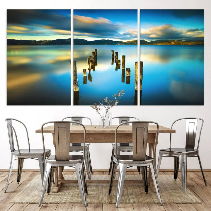 A triptych of a serene lake scene with old wooden pillars, blue sky, and clouds casts a coastal ambiance. The Sea Ocean Sunset Beach Wall Art Canvas Print reflects the soothing nature of the ocean.