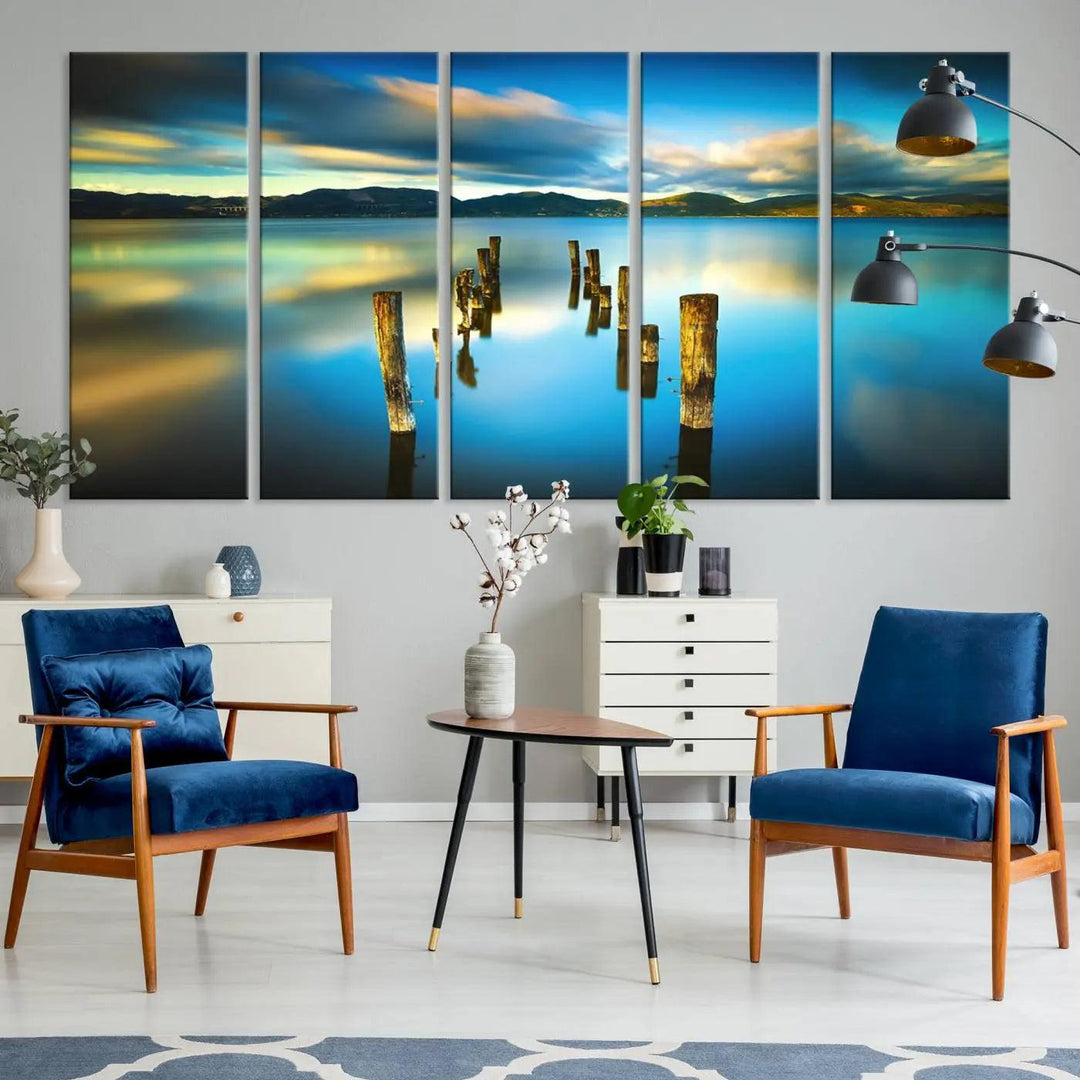 A triptych of a serene lake scene with old wooden pillars, blue sky, and clouds casts a coastal ambiance. The Sea Ocean Sunset Beach Wall Art Canvas Print reflects the soothing nature of the ocean.