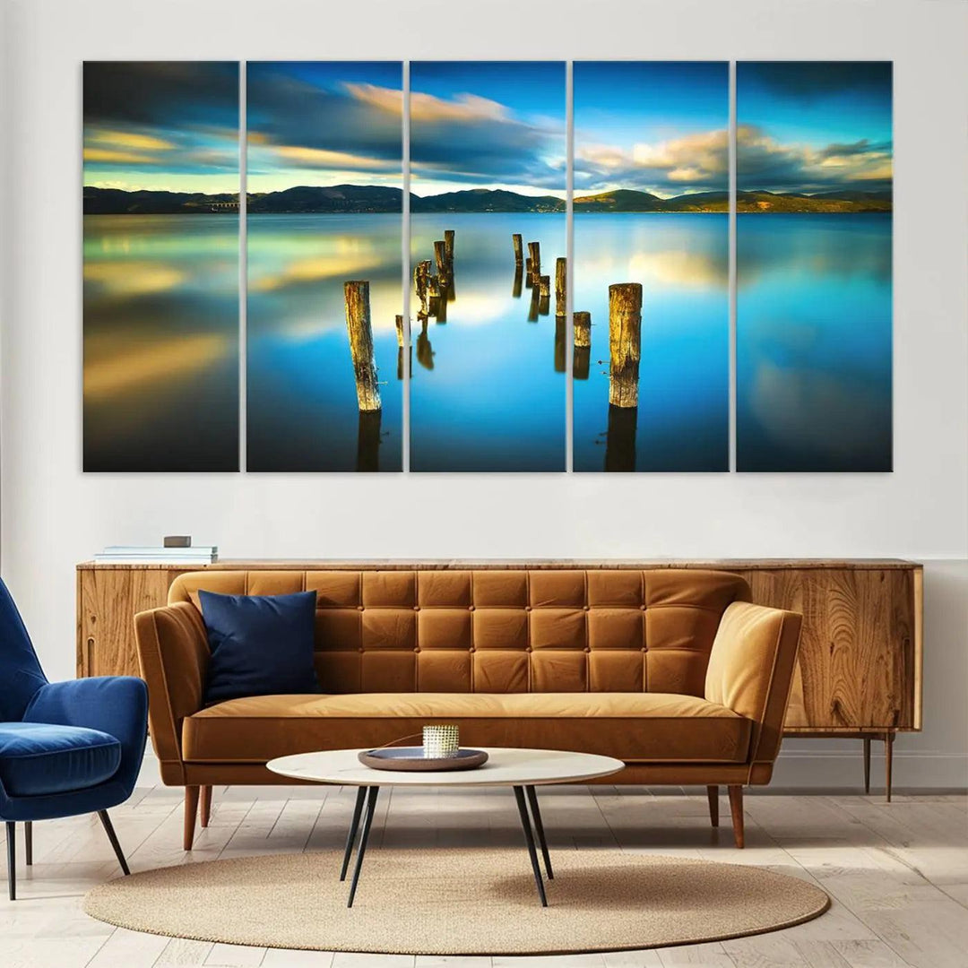 A triptych of a serene lake scene with old wooden pillars, blue sky, and clouds casts a coastal ambiance. The Sea Ocean Sunset Beach Wall Art Canvas Print reflects the soothing nature of the ocean.