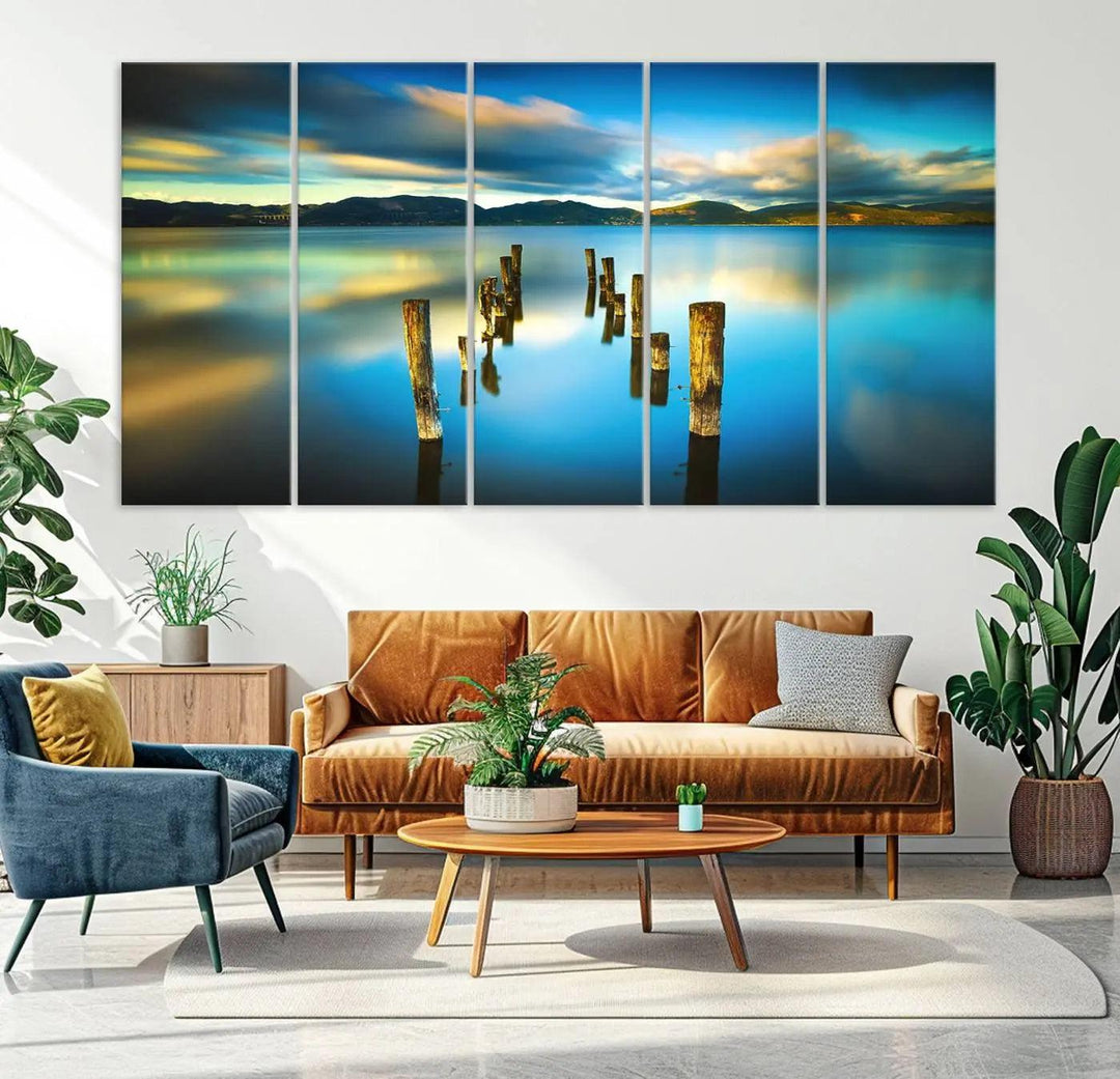 A triptych of a serene lake scene with old wooden pillars, blue sky, and clouds casts a coastal ambiance. The Sea Ocean Sunset Beach Wall Art Canvas Print reflects the soothing nature of the ocean.