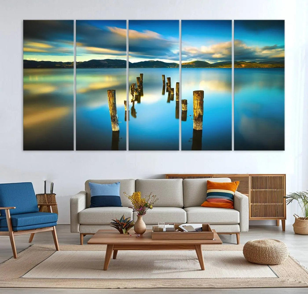 A triptych of a serene lake scene with old wooden pillars, blue sky, and clouds casts a coastal ambiance. The Sea Ocean Sunset Beach Wall Art Canvas Print reflects the soothing nature of the ocean.