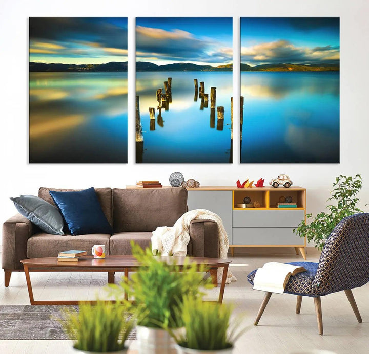 A triptych of a serene lake scene with old wooden pillars, blue sky, and clouds casts a coastal ambiance. The Sea Ocean Sunset Beach Wall Art Canvas Print reflects the soothing nature of the ocean.